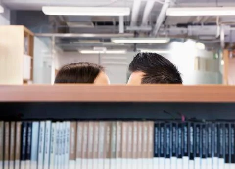 Work romance between two business people hiding behind shelves Stock Photos