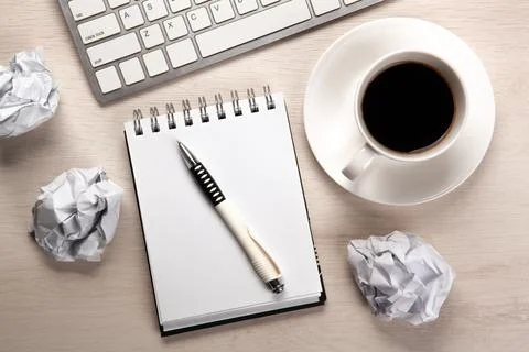 Work table, a cup of coffee, a notebook with a pen and crumpled paper Foto stock