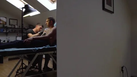 Work tattoo artist with a client lying on couch during a tattoo creation Stock Footage 82840099