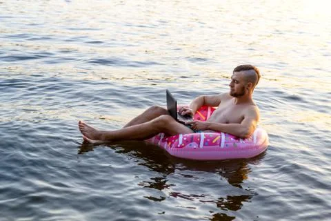Workaholic man working on a laptop while sitting on an inflatable ring, copy  Stock Photos