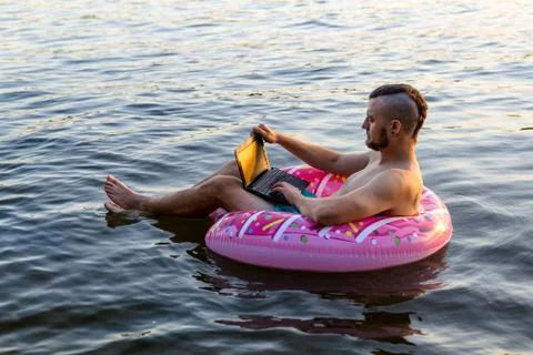 Workaholic man working on a laptop while sitting on an inflatable ring, copy  Stock Photos