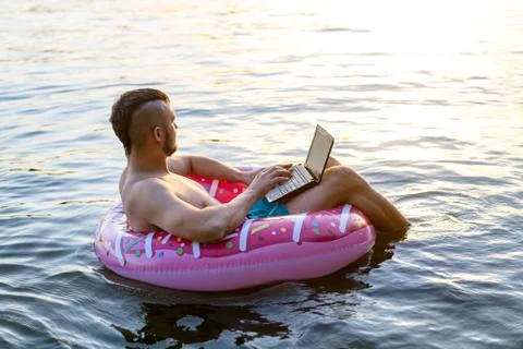 Workaholic man working on a laptop while sitting on an inflatable ring, copy  Stock Photos