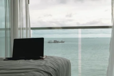 Workation concept. Empty screen laptop on bed and ocean view balcony. Фото