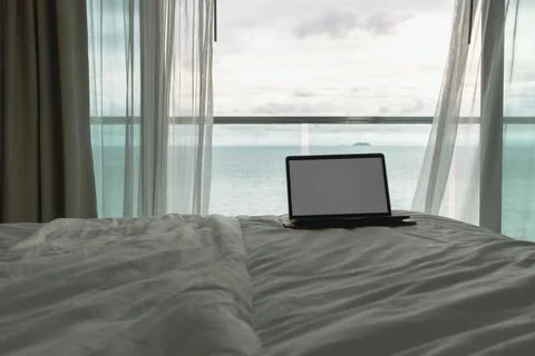 Workation concept. Empty screen laptop on bed and ocean view balcony. Foto stock