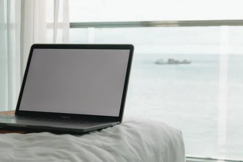 Workation concept. Empty screen laptop on bed and ocean view balcony. Stock-Fotos