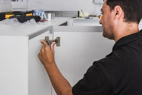 Worker adjusting the hinges of a kitchen cabinet Stock Photos