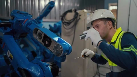 Worker adjusts blue robotic arm with care Stockbeeldmateriaal 344919866
