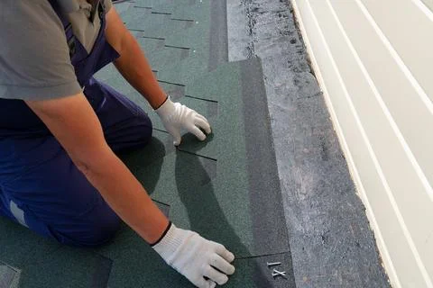 A worker aligns a flexible bituminous shingle before securing it to the roo.. Stock Photos