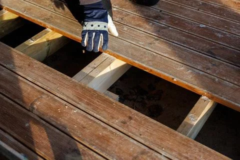 Worker aligns grooved timber deck board on joists during daylight Stock Photos