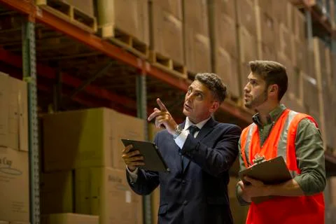 Worker and businessman with digital tablet and clipboard in warehouse Stock Photos