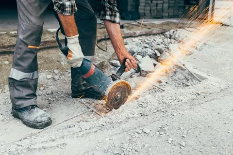 A worker with an angle grinder cuts the concrete pavement of the road, and Stock Photos