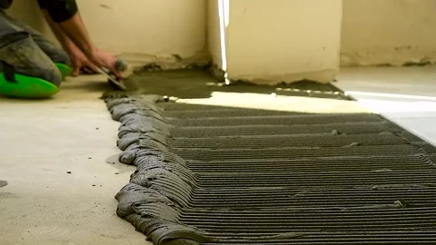 Worker applies cement adhesive to the floor for laying floor tiles. Stock Footage 310052674