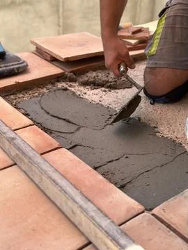 A worker applies cement with a trowel while laying floor tiles during constru Stock Photos