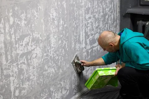 Worker applies plaster to the wall using a trowel and a green tray. Stock Photos