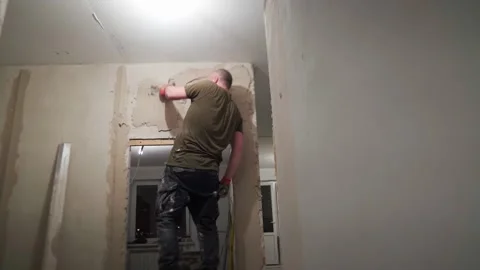 A worker applies a thick layer of plaster while standing on a stepladder Stock Footage 169625079