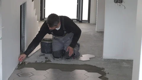 Worker apply glue adhesive on floor and lay hexagon tiles Stock Footage 120508076