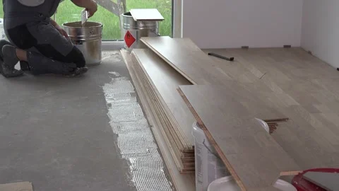Worker apply glue with spatula on floor for floorboard laying Stock Footage 151130197