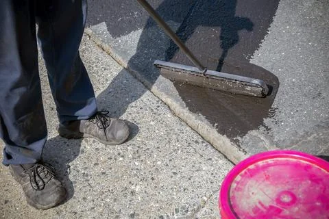 Worker applying asphalt protective coating with roller on driveway surface Stock Photos