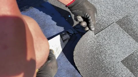 Worker applying bitumen mastic beneath asphalt shingles at seam Stock Footage 346778609