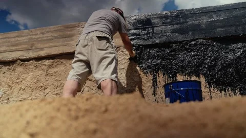 Worker applying black mastic waterproofing coating to foundation Stock Footage 341294332
