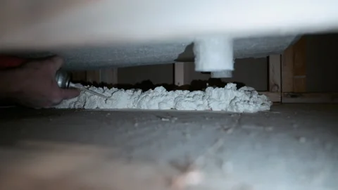 Worker applying expanding foam insulation under bath tube. Construction or Stock Footage 332185860