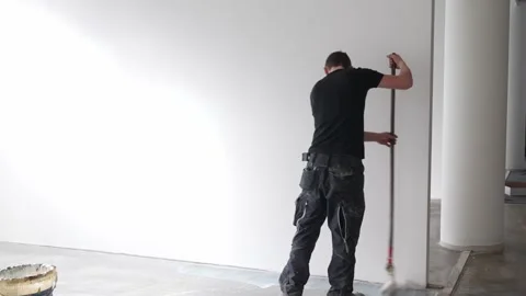 Worker applying floor coating along wall edge in office interior Stock Footage 332811299