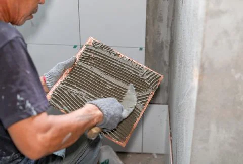 A worker is applying glue cement to wall tiles Stock Photos
