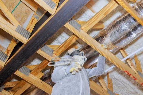 Worker applying insulation in an attic using spray equipment for energy Foto stock