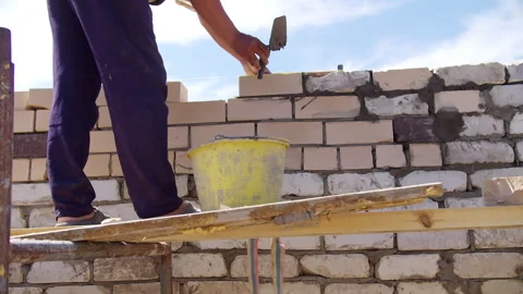Worker applying mortar to brick wall on scaffold Vídeos de archivo 310043120