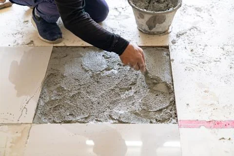The worker is applying mortar to the tile installation area using a trowel. Stock Photos