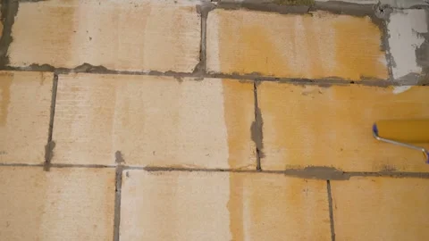 Worker applying orange waterproofing paint with roller on white brick wall Stock Footage 310058336