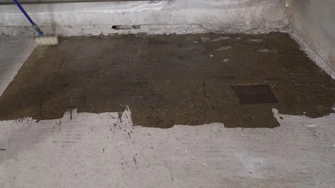 Worker applying primer to concrete floor with paint roller during renovation Stock Footage 345000943