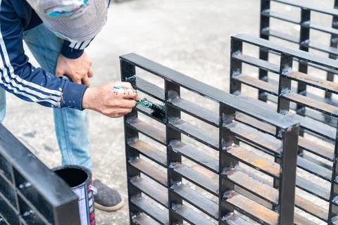 Worker applying protective black paint to the completed metalwork. Foto stock