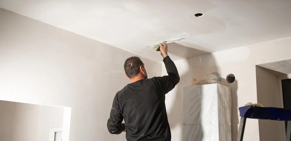 Worker is applying putty on a ceiling. Renovating house Stock Photos