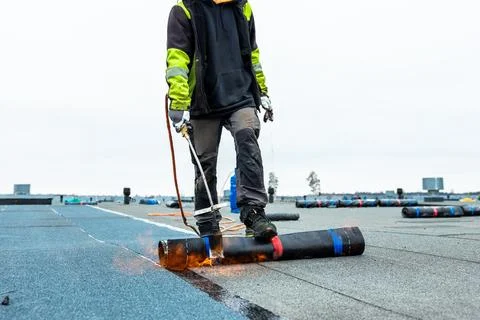 Worker Applying Roofing Material with Torch on Flat Industrial Rooftop Stock Photos