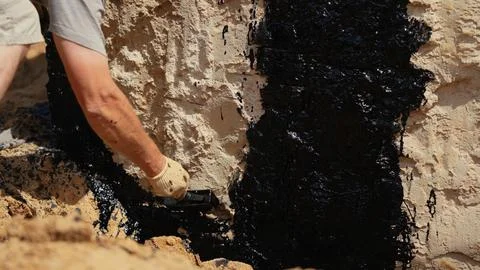 Worker applying waterproofing coating to building foundation wall Stock Photos