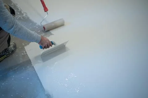 Worker Applying White Liquid Floor Coating With Roller and Trowel Stock Photos