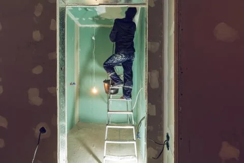 Worker are putting up the ceiling from ladder in apartment is under construction Stock-Fotos