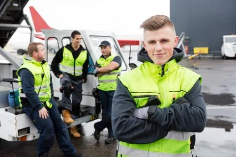 Worker With Arms Crossed Standing While Colleagues Communicating Foto stock