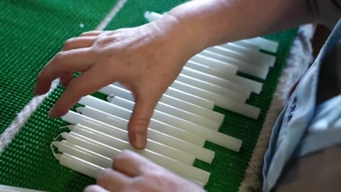 Worker arranging rows of tapered candles on a green mesh mat beside branded Stock Footage 343370604