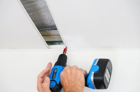 Worker assemble a suspended ceiling and fixing panel with an screwdriver. Stock Photos