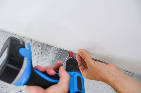 Worker assemble a suspended ceiling and fixing panel with an screwdriver. Stock Photos