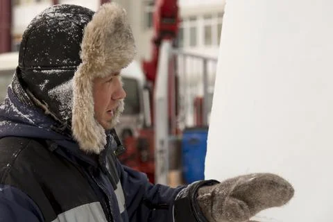 Worker assembler in blue jacket and fur hat at construction site 스톡 사진