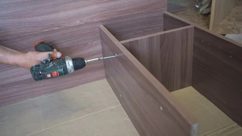 Worker assembles and twists the wooden table with a screwdriver and special scre Stock Footage 108465326