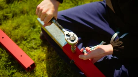 Worker assembling metal frame with ratchet wrench on red beam outdoors. DIY Stock Footage 336310319