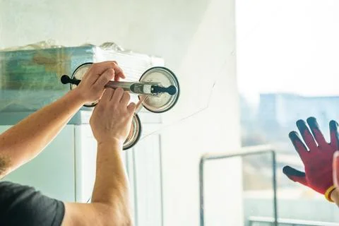 Worker attaching suction cup lifters to cracked window glass before removal from Stock Photos