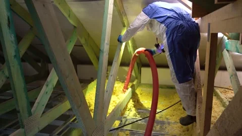 Worker in attic sprays blown insulation into floor between supporting wood beams Vidéo 312325934