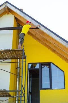 Worker balances on upper scaffold attaching horizontal plank under gable, y.. 스톡 사진