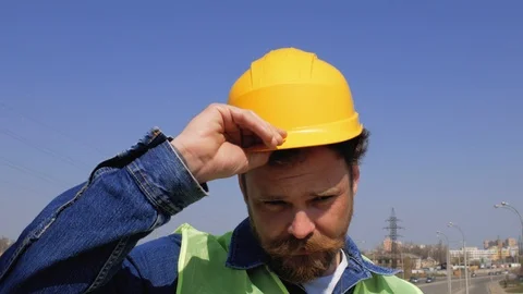 Worker with a beard and mustache smokes a cigarette and puts on a yellow helmet Stock Footage 106356568