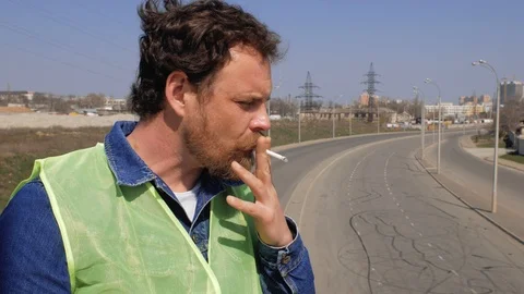 Worker with a beard smokes on a bridge on the background of the autobahn Видео 106356459